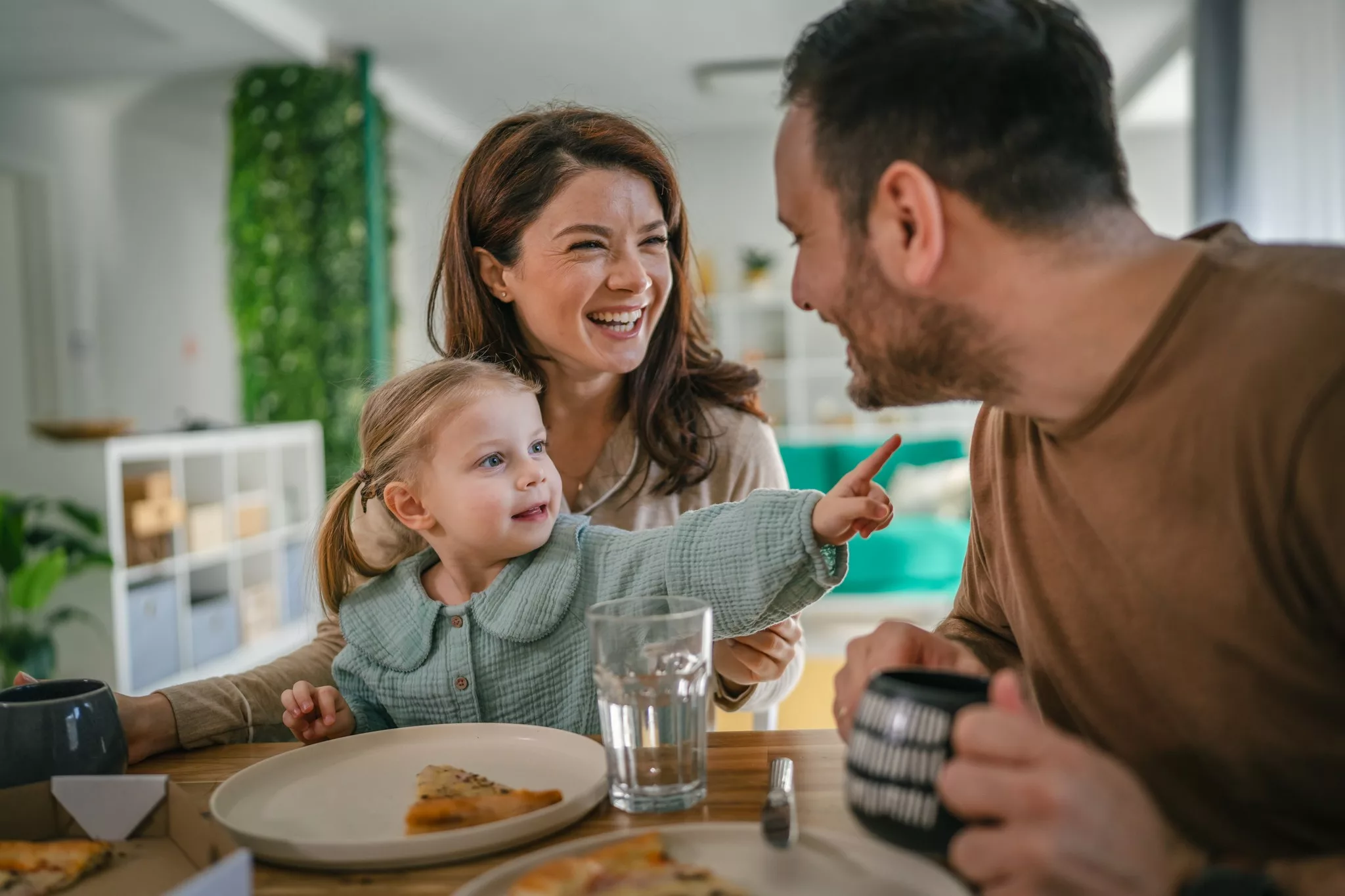 Happy little girl pointing to her father sitting with mom at table